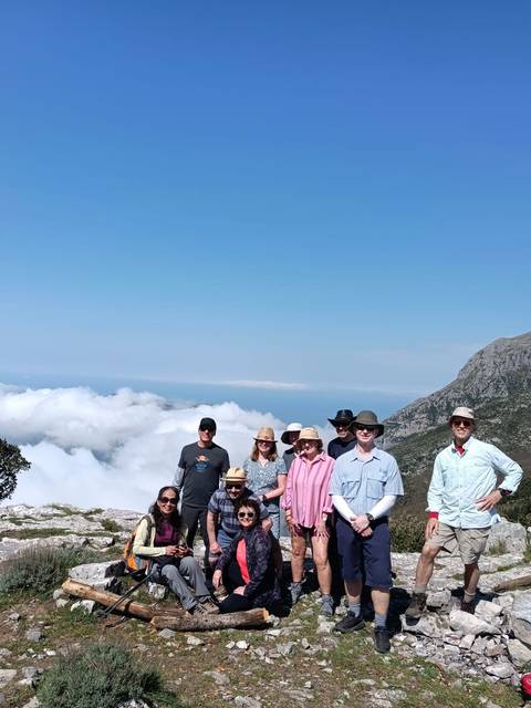       Partially cropped group photo of hikers with blue sky and coastal clouds in the background
  