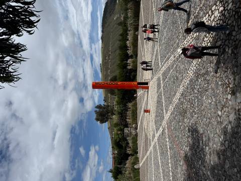       Open plaza at the Mitad del Mundo monument with visitors standing on the equatorial line.
  