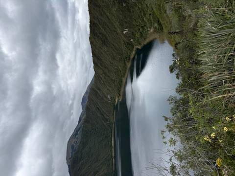       Serene lake surrounded by green hills under a blanket of grey clouds.
  