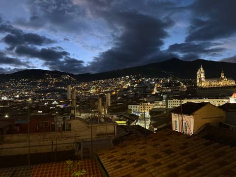       Night panorama of Quito’s twinkling lights with illuminated basilica and mountain silhouette.
  
