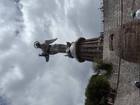      Close-up view of the towering Virgin of El Panecillo statue against a dramatic cloudy sky.
  