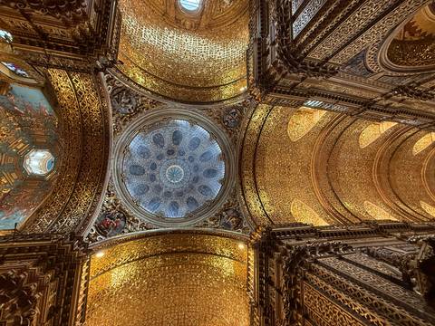       Golden ornate church ceiling with a blue starry dome centerpiece framed by intricate carvings.
  
