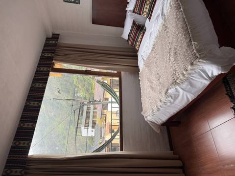       Simple hotel room with a hammock view toward green hills through a large window.
  