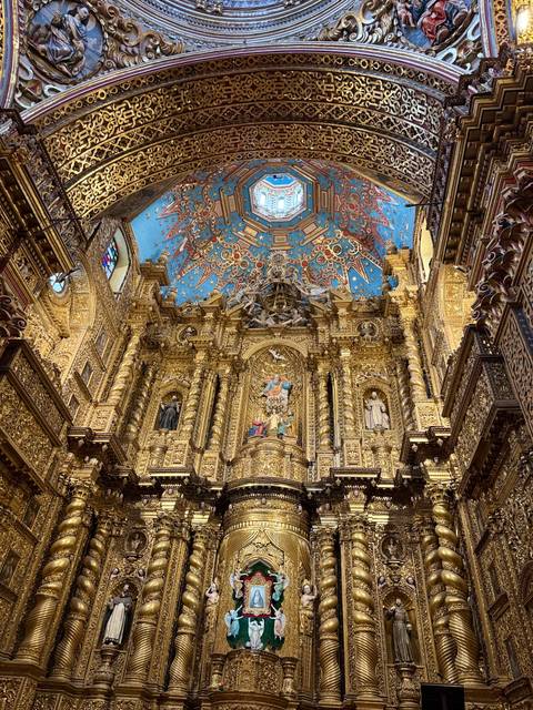       Magnificent gilded altar with vivid blue ceiling painted with stars inside an ornate church.
  