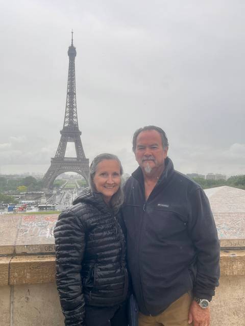       Smiling couple posing on a misty day with the Eiffel Tower rising behind them.
  