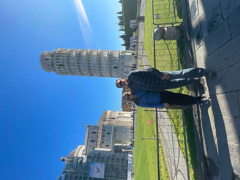       Couple posing in front of the Leaning Tower of Pisa and cathedral on a bright blue day.
  
