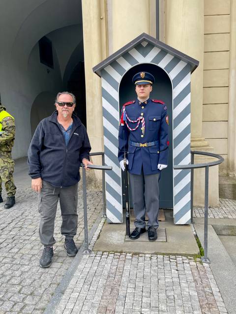       Male tourist standing beside an immobile ceremonial guard at Prague Castle entrance.
  