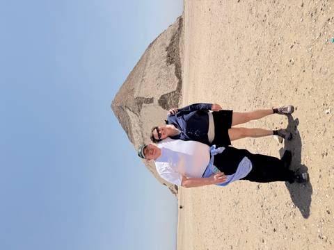       Smiling couple posing in front of Egypt’s distinctive Bent Pyramid on a bright desert day.
  