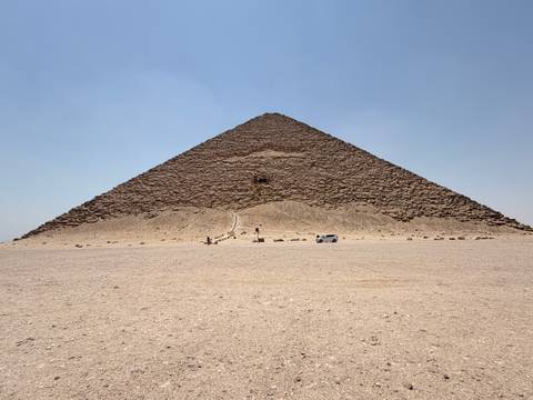       Symmetrical frontal view of the Bent Pyramid rising from the sandy desert plain.
  