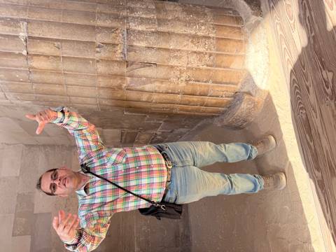       Tour guide gesturing enthusiastically beside ancient stone columns inside an Egyptian monument.
  