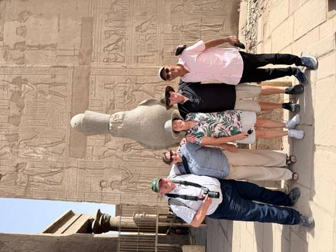       Five travellers smiling in front of hieroglyphic-covered walls at an Egyptian temple.
  