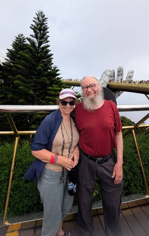       Couple posing in front of Vietnam’s iconic Golden Bridge with giant stone hands supporting the walkway.
  