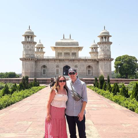       Couple standing together in front of the ornate Itimad-ud-Daulah mausoleum on a bright day.
  