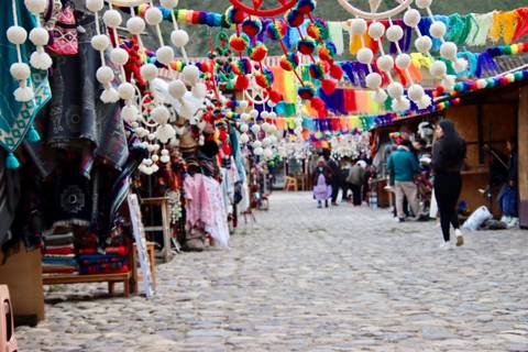       Colorful Andean craft market street with hanging pom-pom decorations and shoppers on a cobblestone lane
  