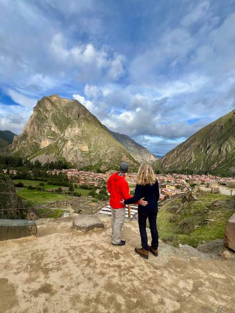       Couple admiring the panoramic view of Ollantaytambo ruins and steep green mountains
  