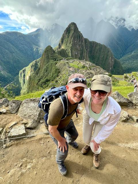       Couple posing with the iconic terraces and peaks of Machu Picchu spread out behind them
  