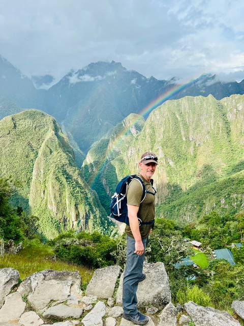      Hiker with backpack standing on a lush mountain ridge under a rainbow
  
