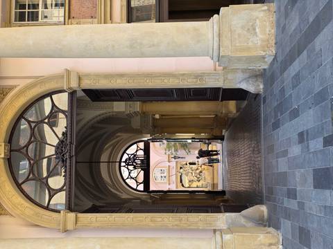       Historic archway leading to a courtyard where two people admire a baroque fountain sculpture.
  