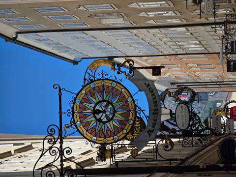       Decorative wrought-iron shop sign with colourful compass motif hanging over a narrow European street.
  