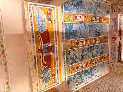       Colorful winged sun disc and hieroglyphic panels decorate the plaster ceiling of an Egyptian tomb.
  