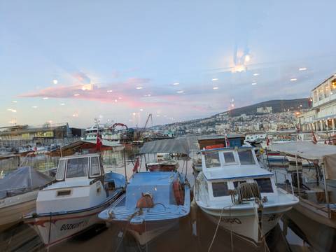       Evening view of small fishing boats moored in a city marina with pink clouds reflected in the glass window.
  