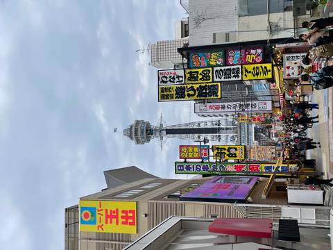       Neon-lined shopping street leading to the Tsutenkaku Tower rising above colourful signboards in Osaka.
  