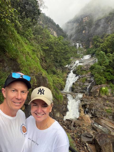       Couple poses before a tall cascading jungle waterfall in Sri Lanka.
  