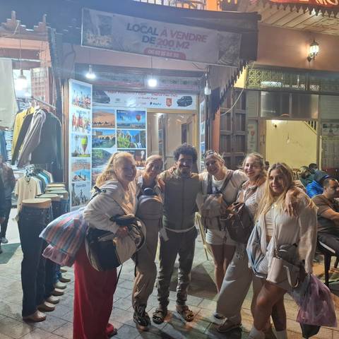       Group of cheerful travelers posing outside a brightly lit souvenir shop at night
  