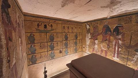       Colorful wall paintings adorn an ancient Egyptian tomb chamber surrounding a stone sarcophagus.
  