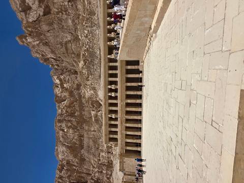       The terraced facade of Hatshepsut’s Temple nestles beneath towering desert cliffs under a deep blue sky.
  
