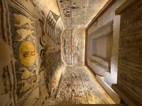       An elaborately painted burial chamber with sunken floor lies illuminated within an Egyptian tomb.
  