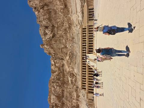       Tourists approach the grand Temple of Hatshepsut against towering desert cliffs.
  