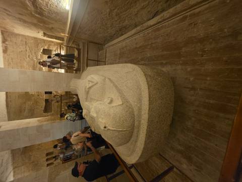       Visitors view a large stone sarcophagus displayed inside an ancient Egyptian tomb chamber.
  