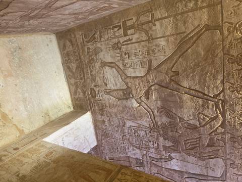       Sunlit relief showing pharaoh defeating enemy on temple wall with rich details.
  