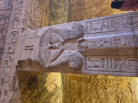       Column capital carved with face of Hathor and hieroglyphs in Egyptian temple interior.
  