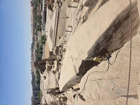       Site of the unfinished obelisk quarry with large cracked stone block and cityscape in background.
  