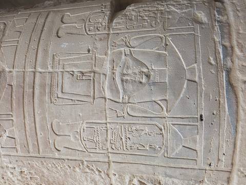       Weathered carving of Hathor-like face and cartouches on temple column surface.
  