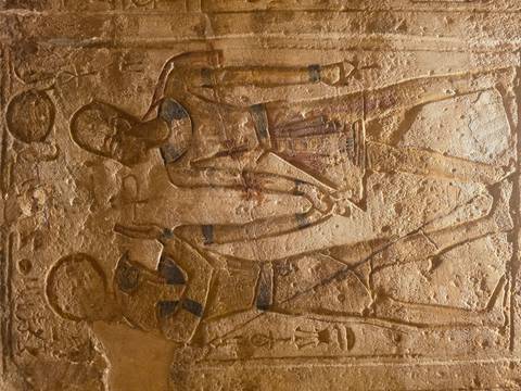       Golden-lit relief showing two ancient Egyptian figures clasping hands.
  