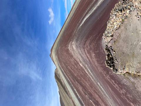       Sharp ridge of Rainbow Mountain displaying maroon and cream mineral layers against blue sky
  