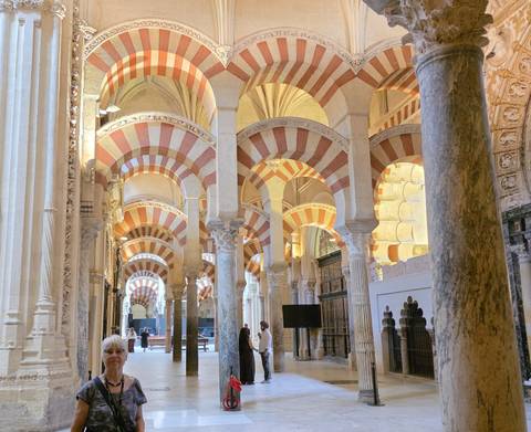       Interior of the Mezquita-Cathedral of Córdoba showing striped horseshoe arches and stone columns under soft lighting.
  