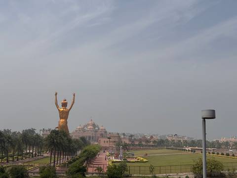       Distant view of the Akshardham temple complex with a large golden statue in the foreground on a hazy day in Delhi.
  