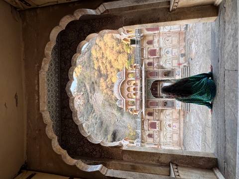       Woman sits framed by an ornate archway overlooking the pastel-coloured Galtaji temple complex.
  