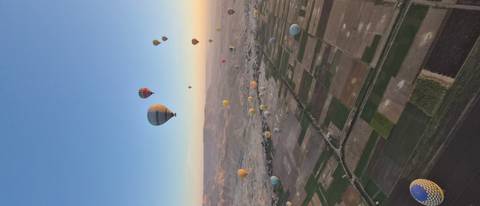       Dozens of hot-air balloons floating over patchwork farmland at sunrise in Luxor
  