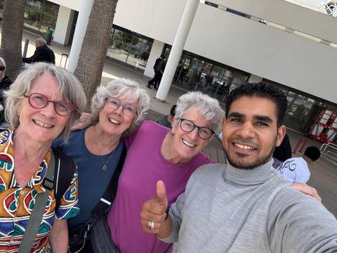       Cheerful group selfie of three senior travellers with local guide giving thumbs up.
  