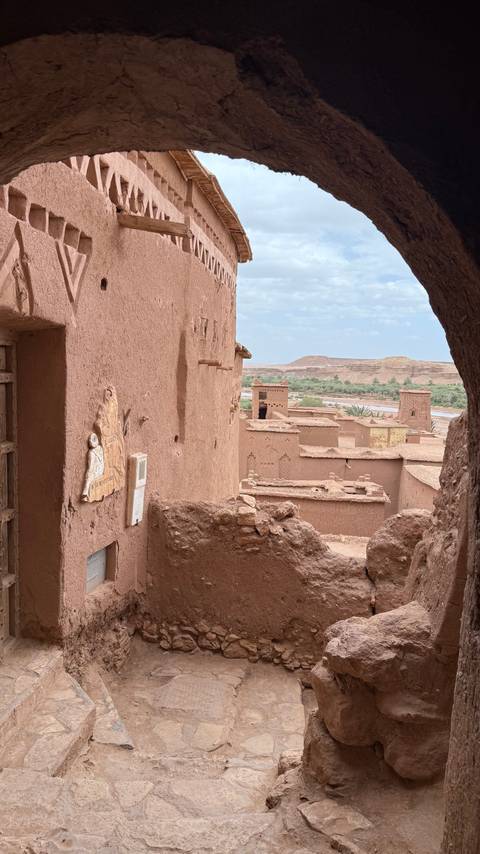       View over the earthen kasbah buildings of Ait Benhaddou with a river and arid hills in the background.
  