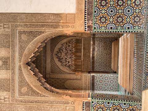       Intricately carved archway and tiled walls inside a historic Moroccan mausoleum.
  