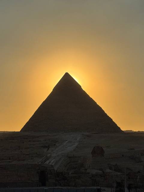       Silhouette of a pyramid perfectly aligned with the glowing golden sun behind at sunset.
  