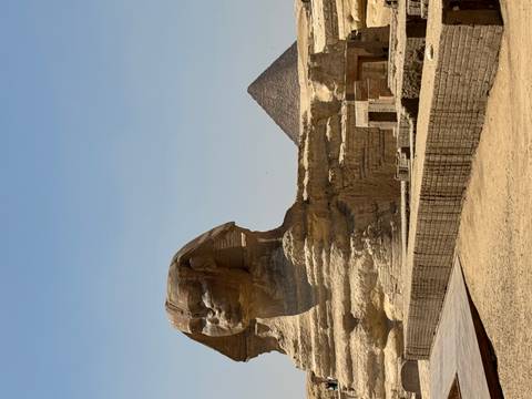       The Great Sphinx of Giza with a pyramid rising behind under a clear desert sky.
  