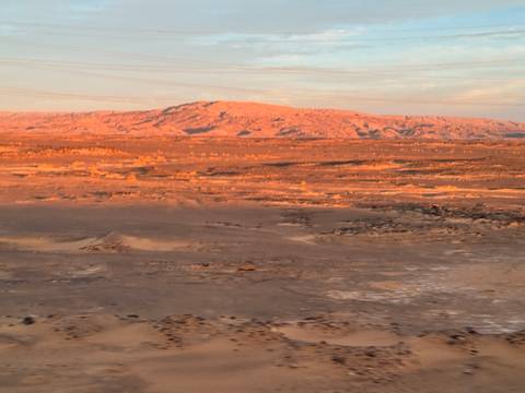       Slightly blurred desert landscape at dusk with soft orange light on distant hills.
  
