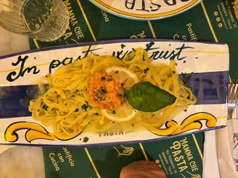       Plate of tagliatelle pasta topped with creamy salmon sauce, basil leaf and lemon slice on decorative ceramic dish
  